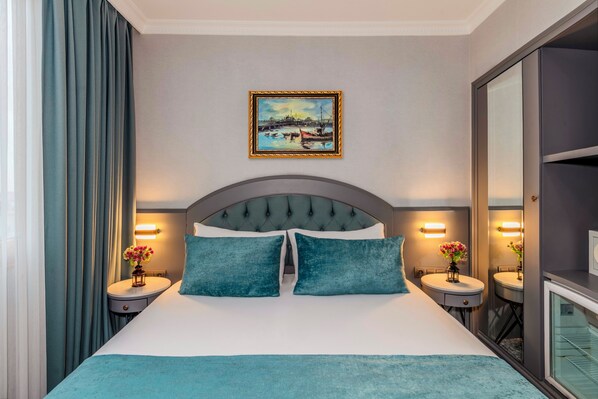 Un cuarto de hotel con una cama grande, dos mesitas de noche con lámparas, un cuadro en la pared y un espejo al lado derecho.