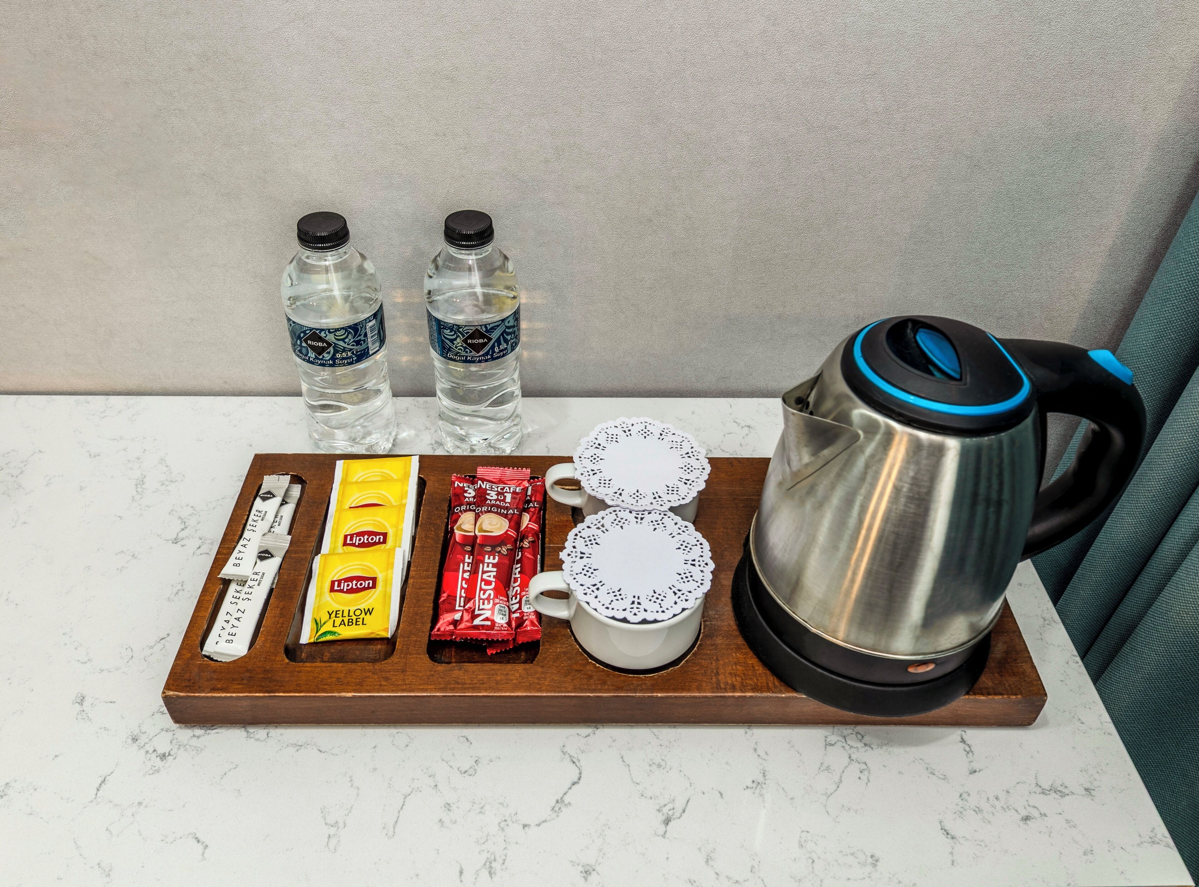 A tray with a coffee maker, two water bottles, a coffee pod, a Lipton tea packet, and two cups on a marble countertop.