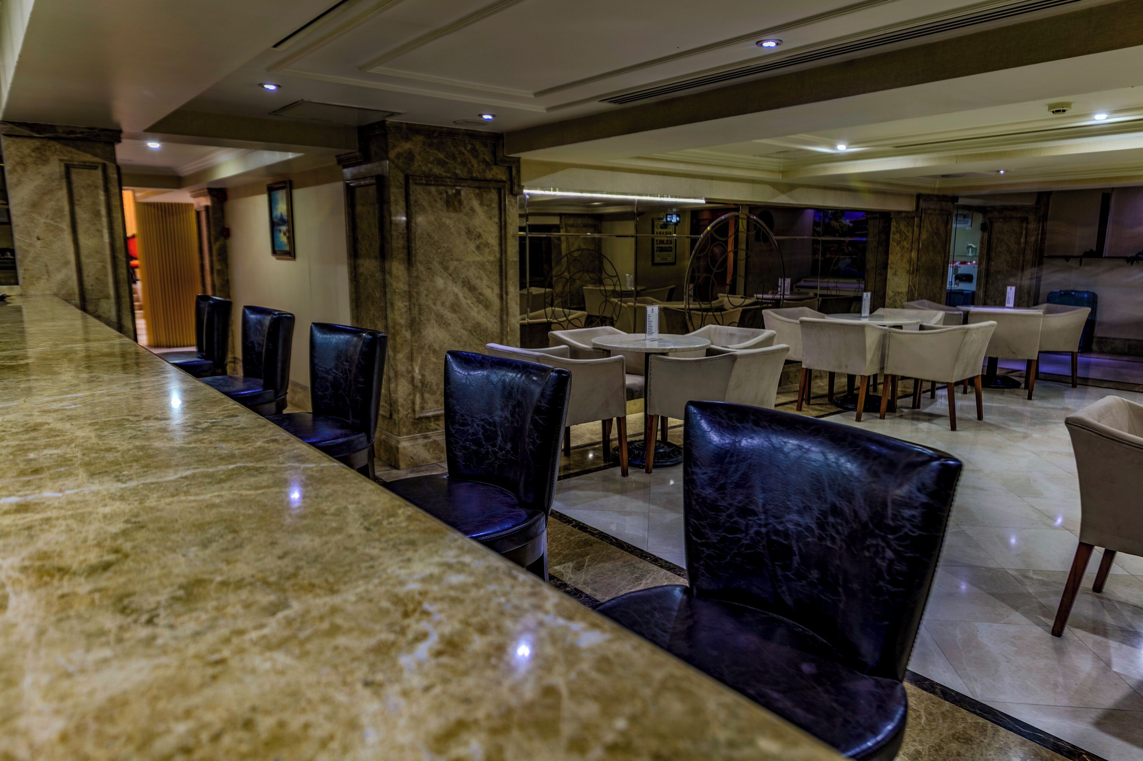 Un hall d’hôtel doté d’un comptoir de réception en marbre, de sièges en cuir et offrant une vue sur le bar.