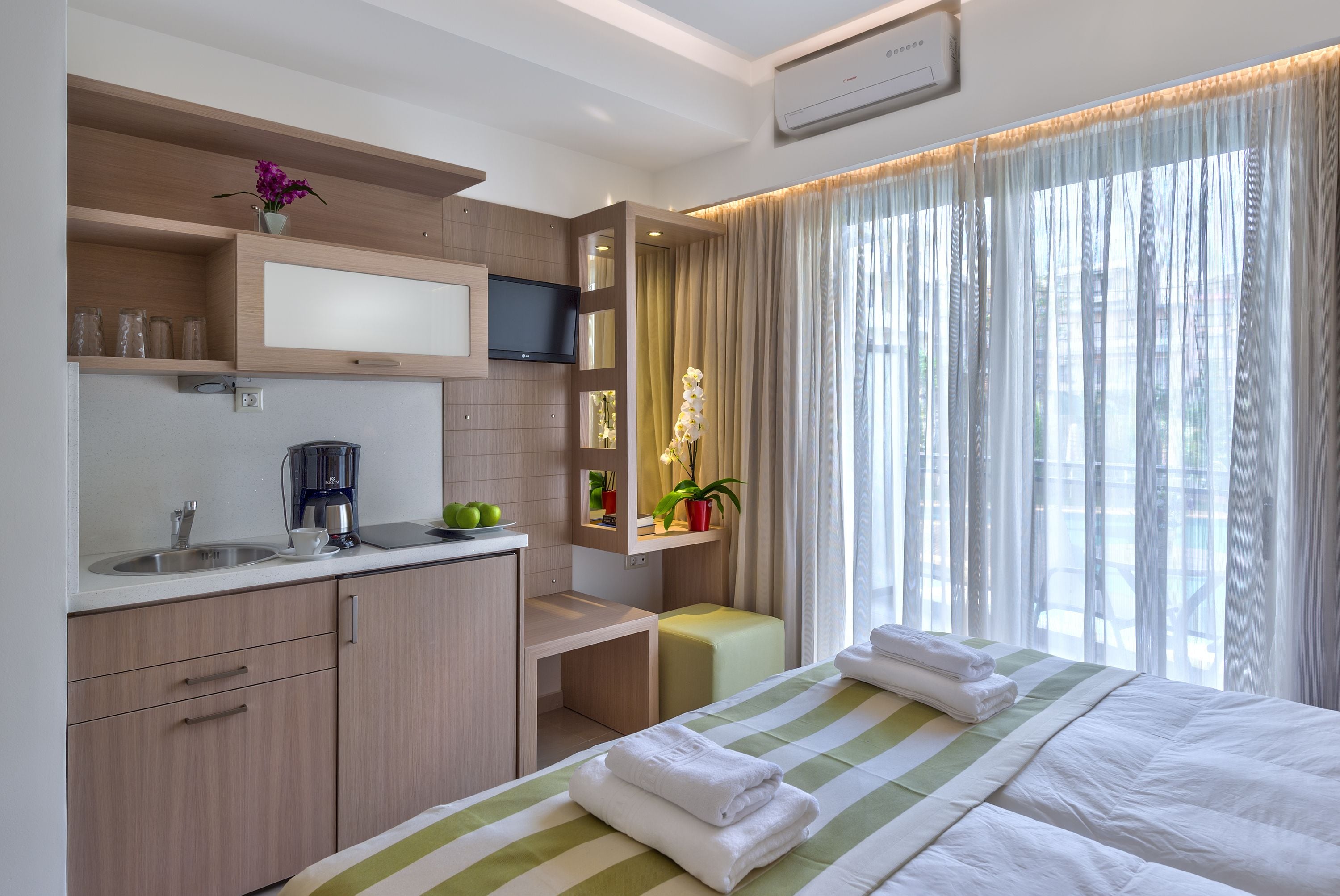 A hotel room with a bed, a desk, a sink, and a window with curtains.