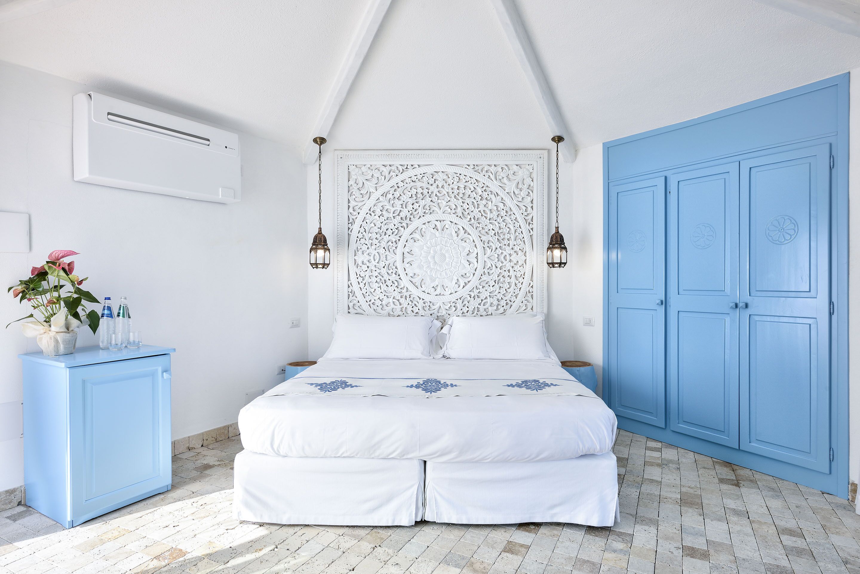 A bedroom with a bed, a blue wardrobe, a white bedside table, and a decorative headboard.