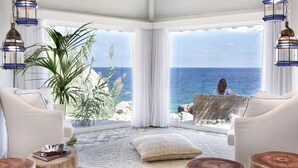 Habitación con vista al mar, que incluye un sofá blanco, una planta grande y faroles colgantes.