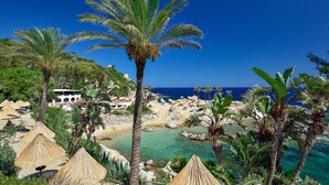 Un resort frente a la playa, con palmeras, agua cristalina y un litoral rocoso.