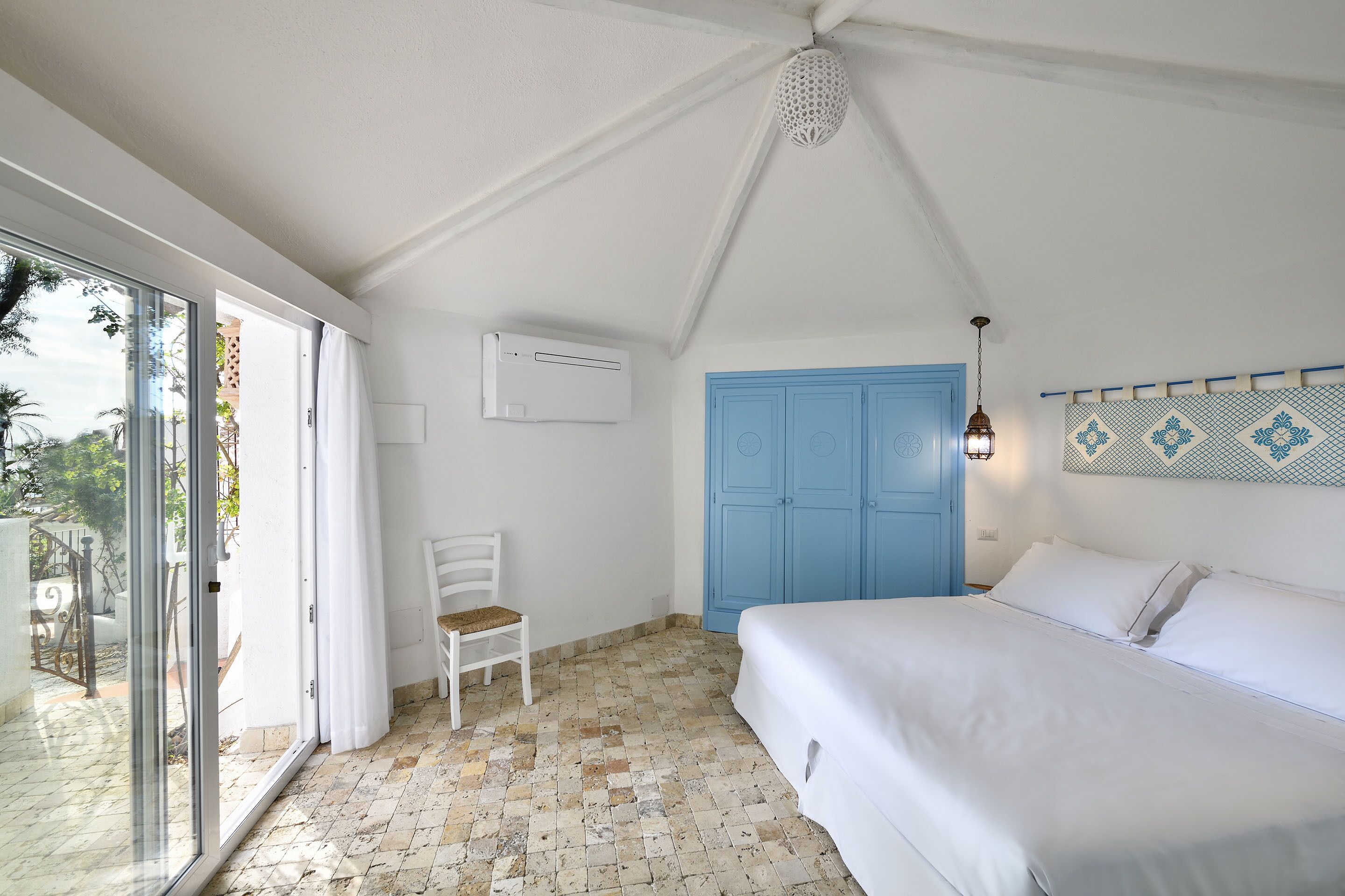 A bedroom with a bed, a chair, a blue door, and a glass door leading outside.