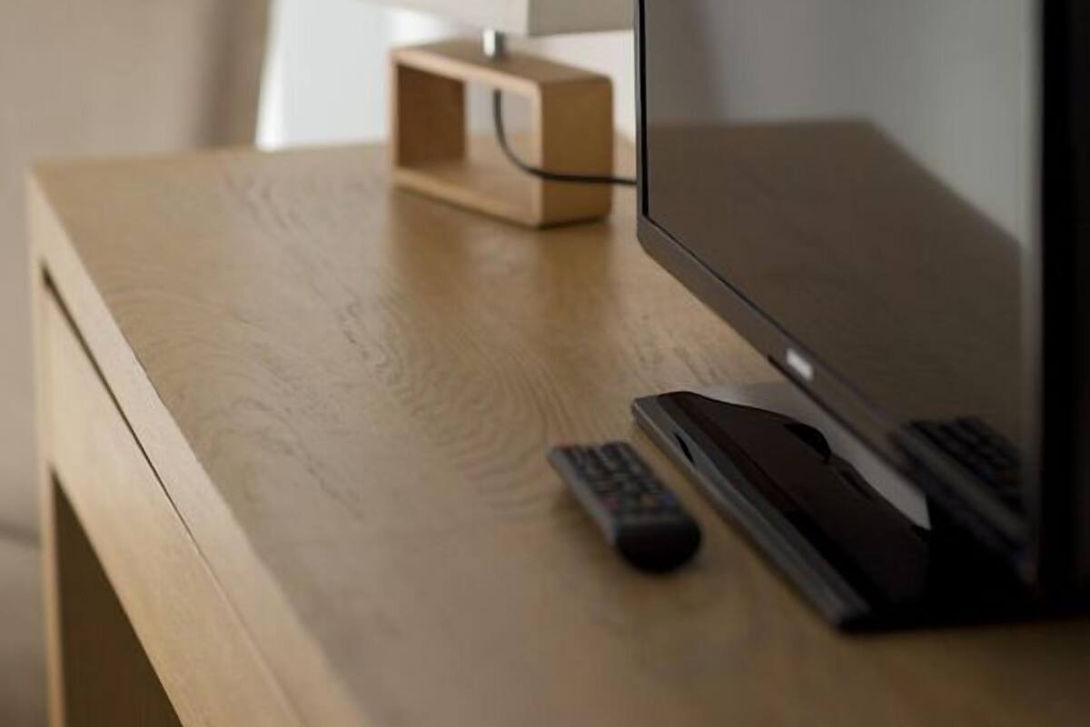 A wooden desk with a flat-screen TV, a remote control, and a lamp.