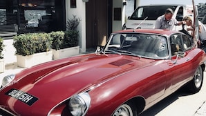 A classic red car parked in front of a modern building with a white facade and large windows. - Le Versailles (Villefranche-sur-Mer)