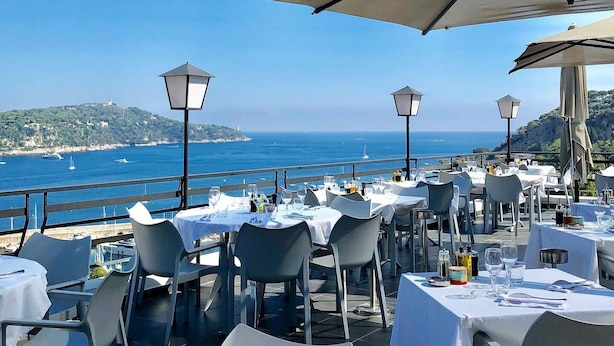 An outdoor dining area with tables set for two, overlooking a coastal view. - Le Versailles (Villefranche-sur-Mer)