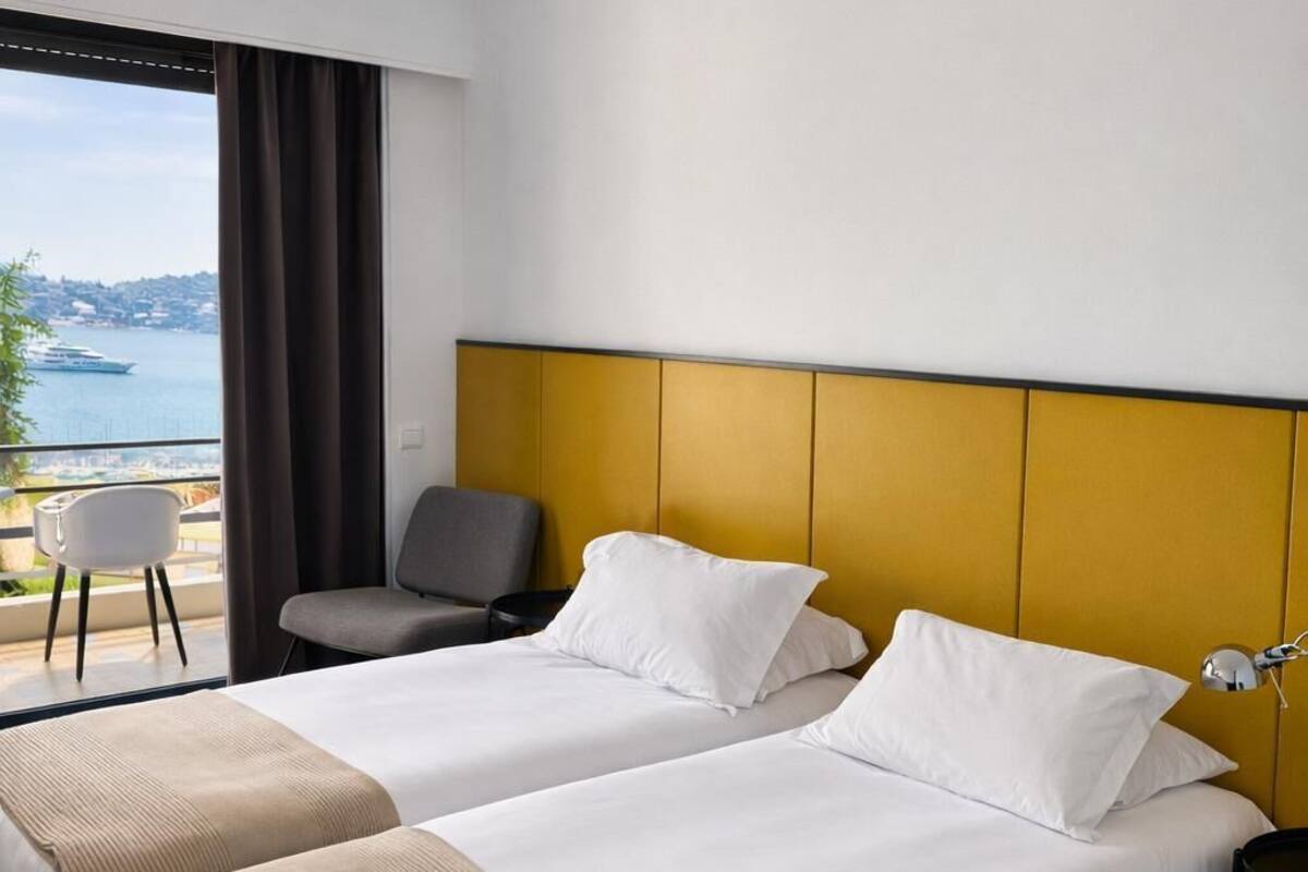 A hotel room with two beds, a view of the sea, a chair, and a nightstand.