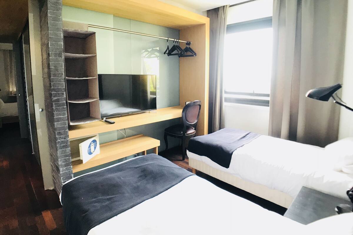 A hotel room with two beds, a desk, a TV, and a wardrobe.