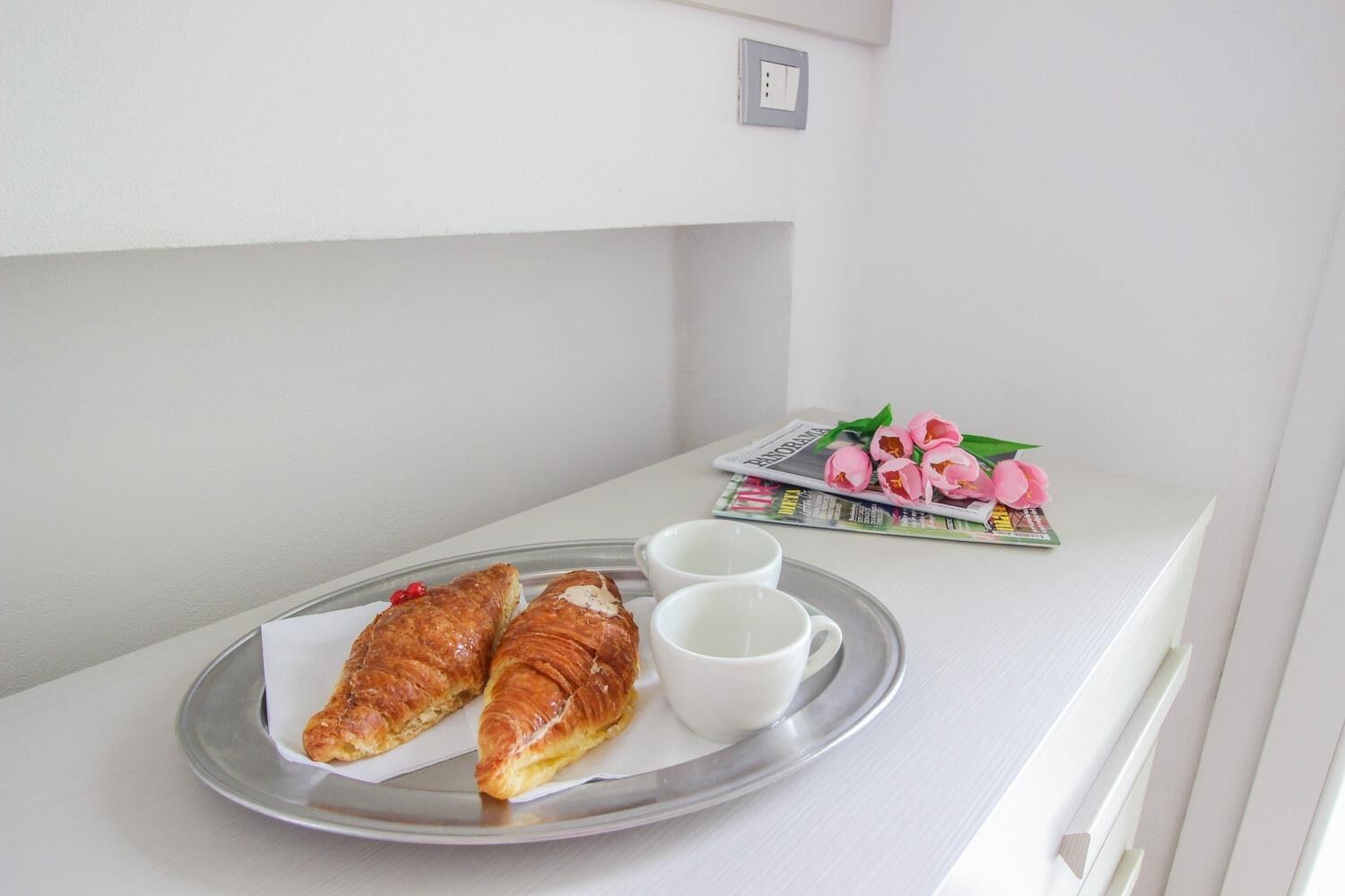 A tray with two croissants and two white cups on a white table.