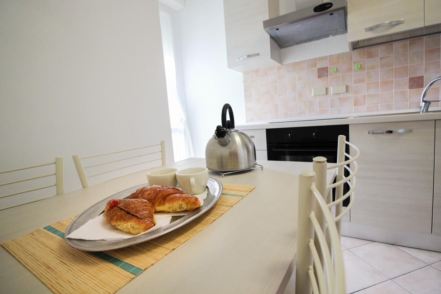 Una colazione con croissant, due tazze e un bollitore su un vassoio.