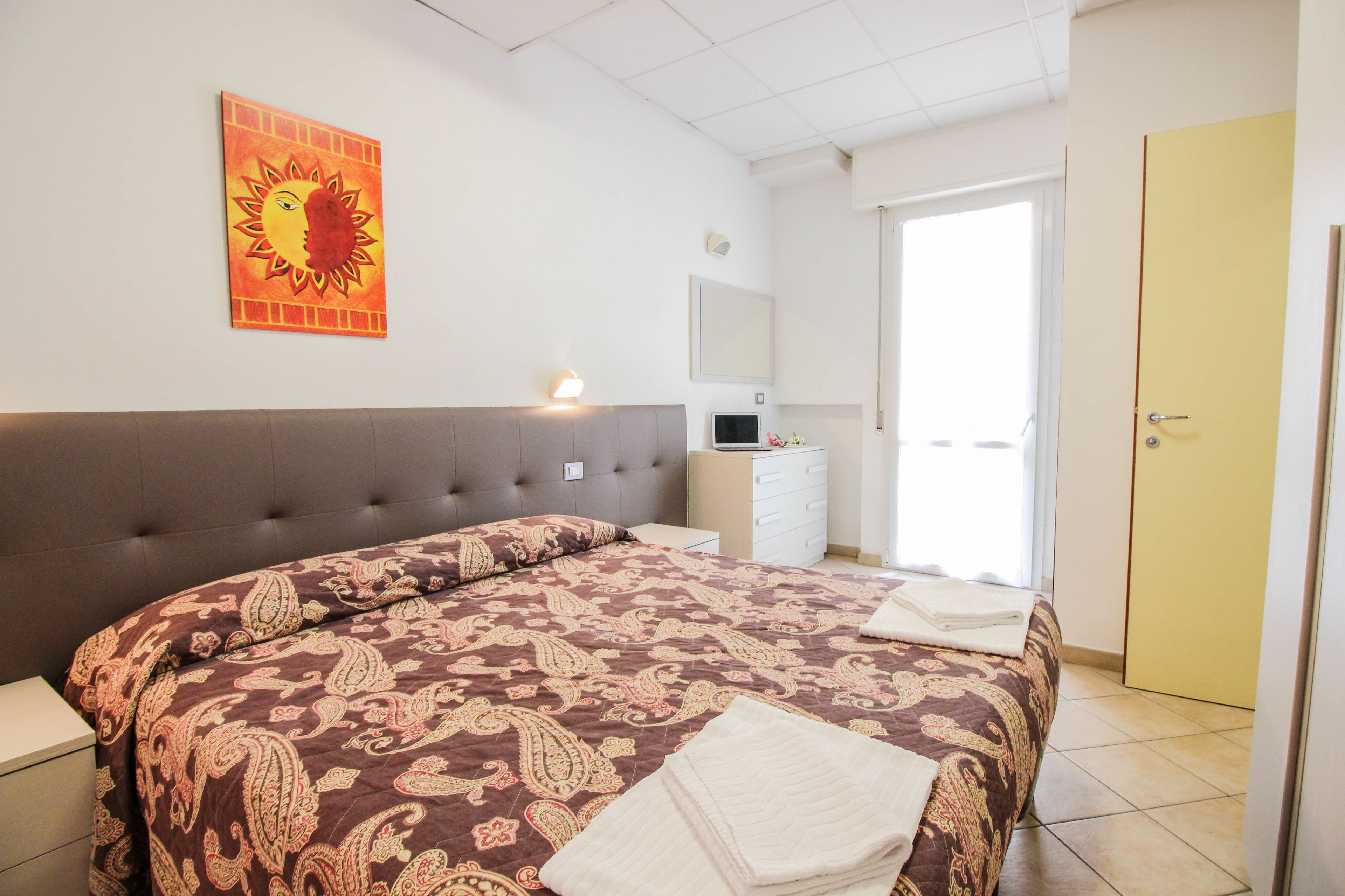 Quarto com uma cama grande, mesa de cabeceira, penteadeira e porta.