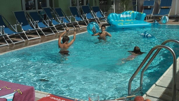 Una piscina con sillas de descanso, un flotador inflable azul y una mesa con una bandeja de frutas y bebidas.