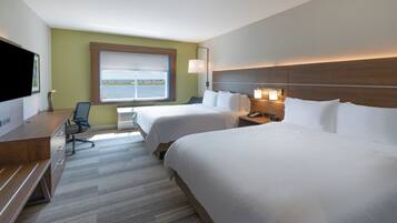 Habitación de hotel con dos camas, un escritorio con silla, televisor y ventana con vista al mar.