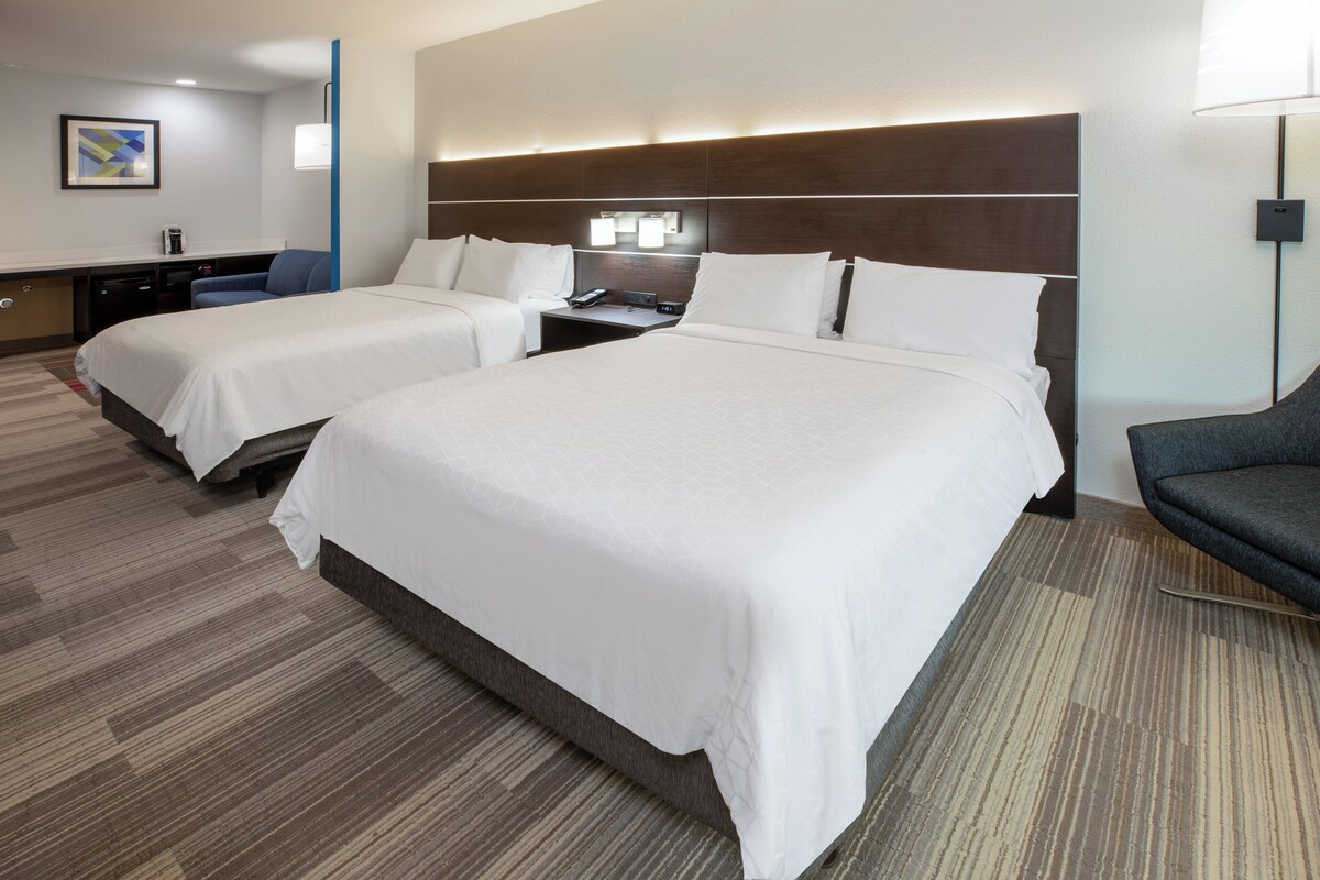 Une chambre d’hôtel avec deux lits, un bureau, une chaise et une lampe.