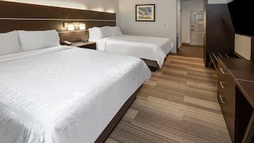 A hotel room with two beds, a wooden headboard, a bedside table with a lamp, and a TV.