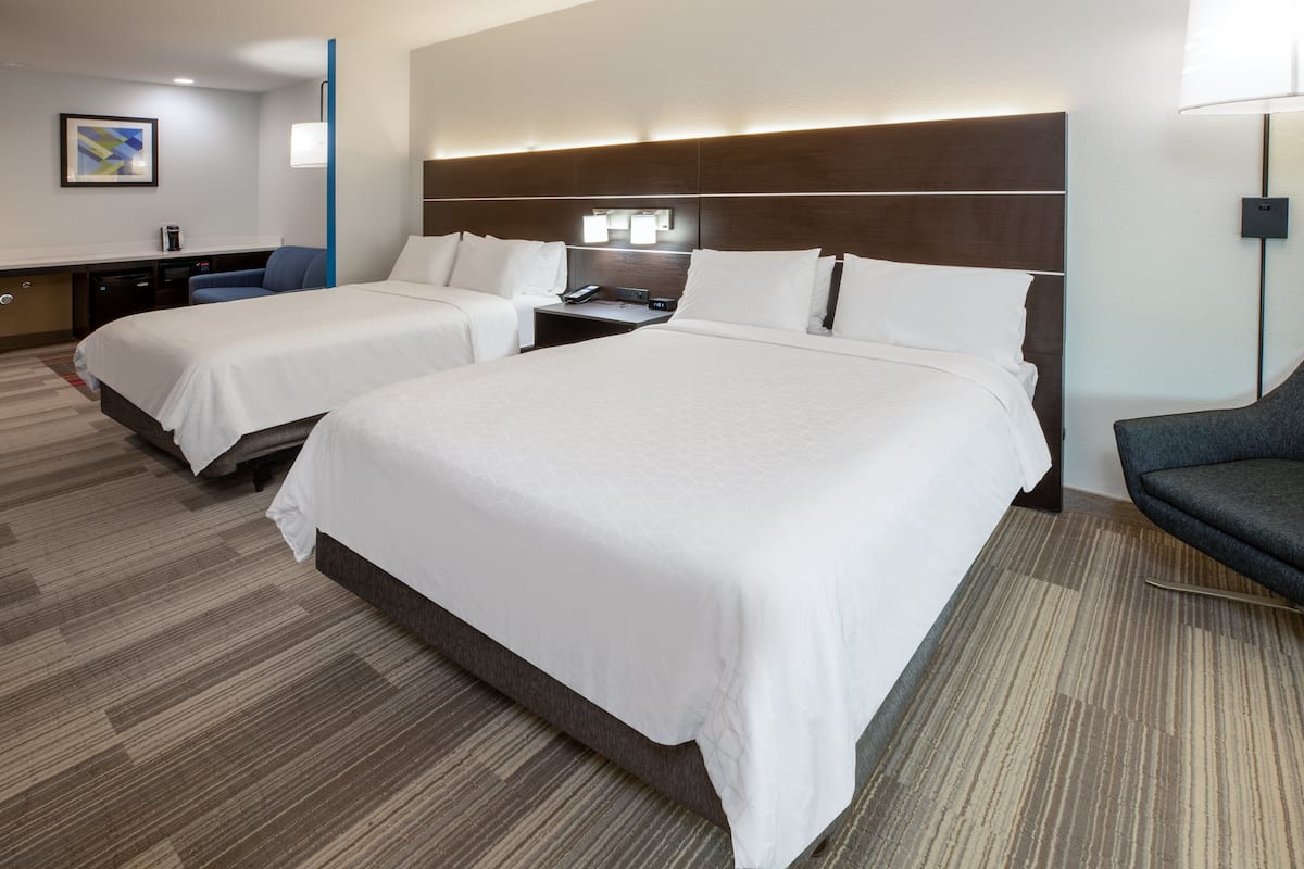 Una habitación de hotel con dos camas, un escritorio, una silla y una lámpara.