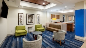 A modern hotel lobby with a blue carpet, green armchairs, a beige sofa, and a dining area with a bar. - Holiday Inn Express & Suites Rockport - Bay View by IHG (Rockport)