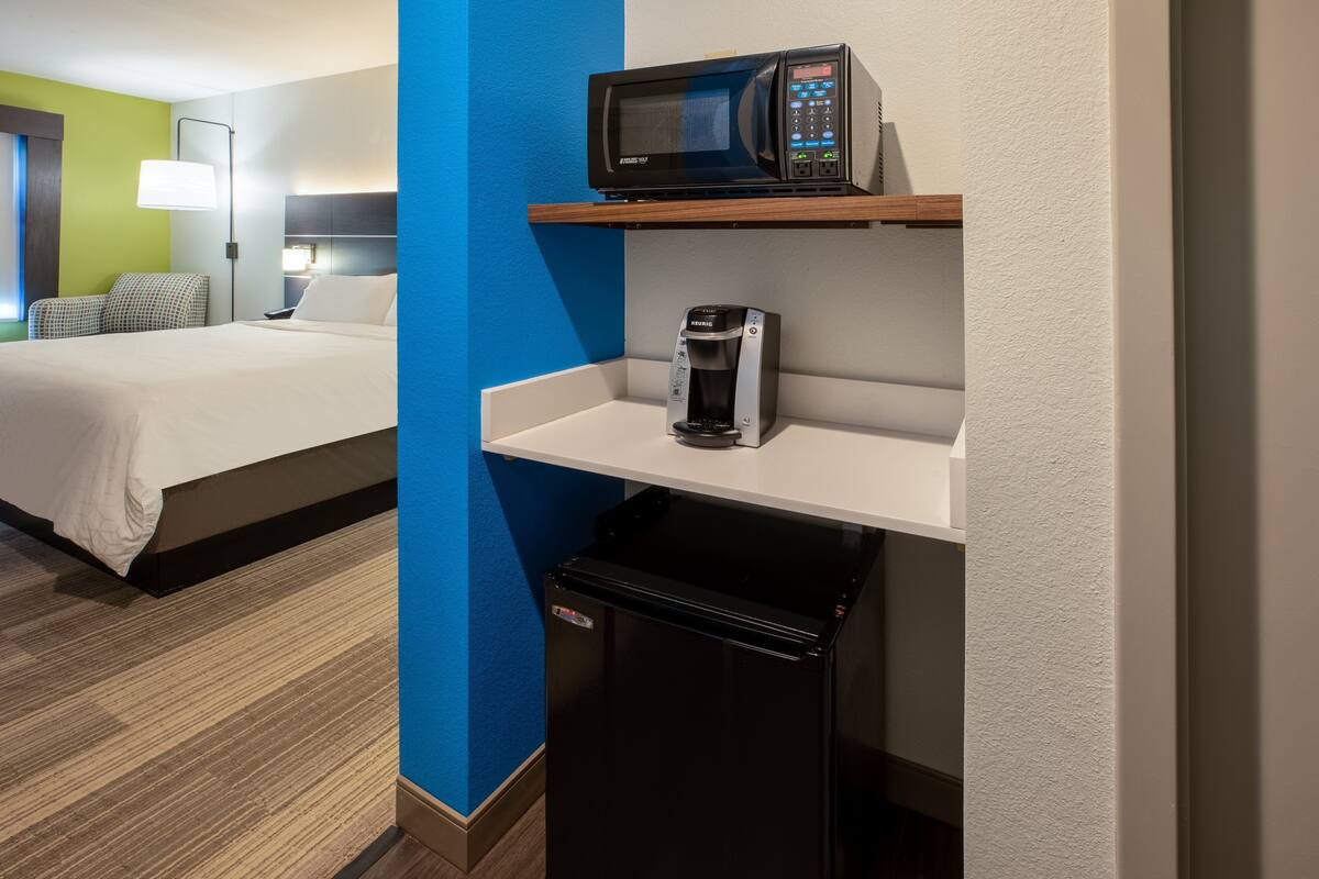 Una habitación de hotel con cama, microondas, cafetera y refrigerador pequeño.