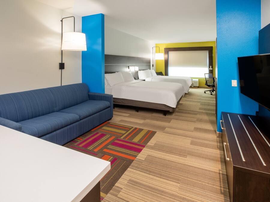 Een hotelkamer met een blauwe bank, een bed met witte lakens, een televisie en een bureau.