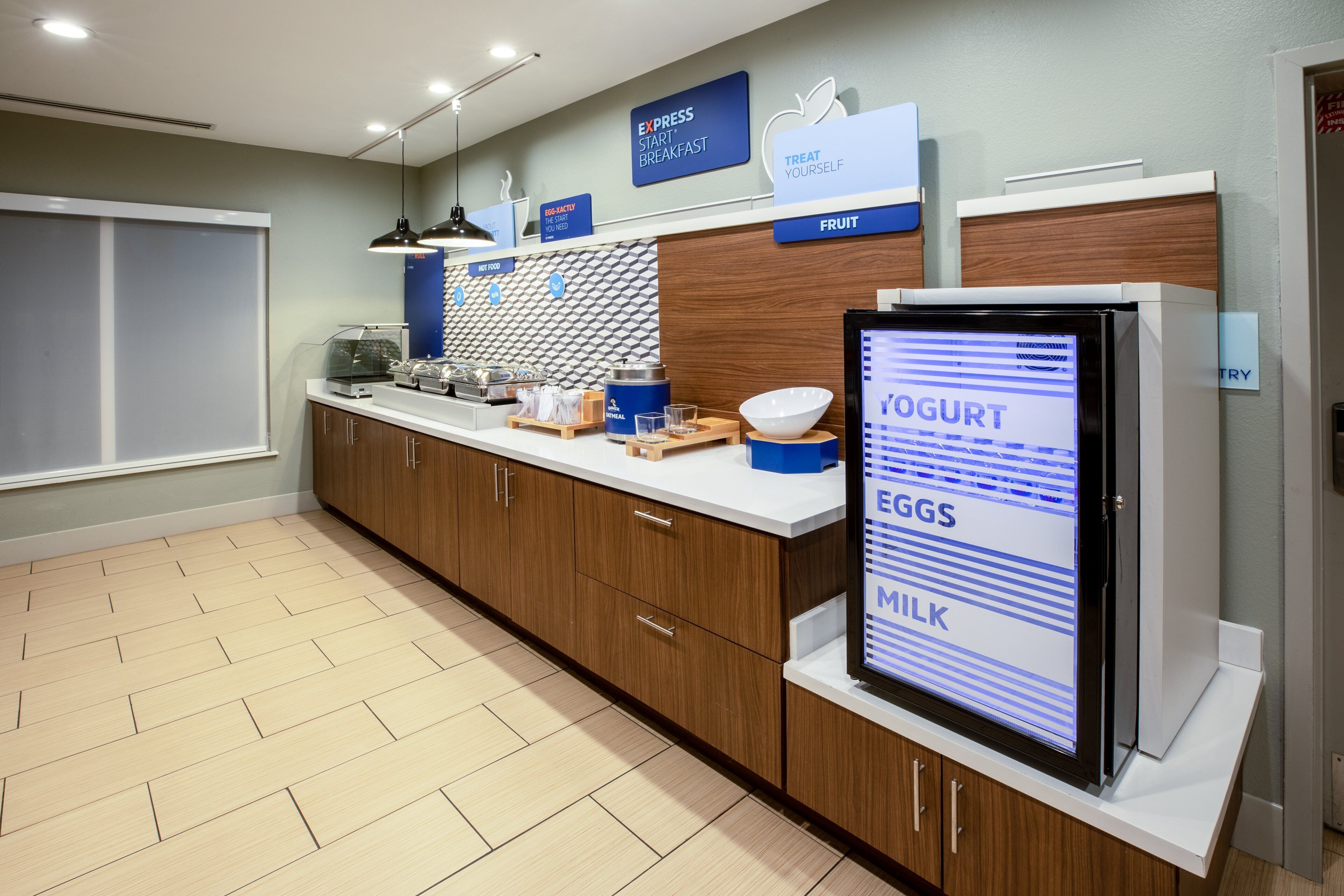 A modern breakfast area with a digital menu display, wooden cabinets, and a clean, tiled floor.