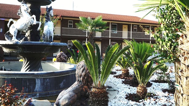 A fountain with horse statues, surrounded by palm trees and a building with balconies in the background. - Savannah Inn and Suites (Garden City)