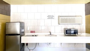 A kitchen with a stainless steel refrigerator, a microwave, and a sink with a cutting board sign. - Savannah Inn and Suites (Garden City)