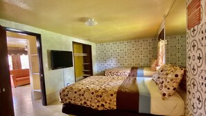 A bedroom with a bed, a TV mounted on the wall, a wardrobe, and patterned wallpaper. - Savannah Inn and Suites (Garden City)