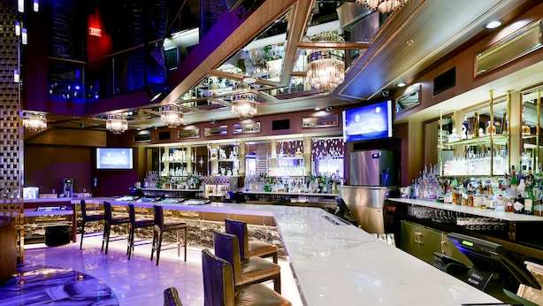 Un bar con varias zonas de estar, una pantalla de televisión y una variedad de botellas y copas en estanterías.
