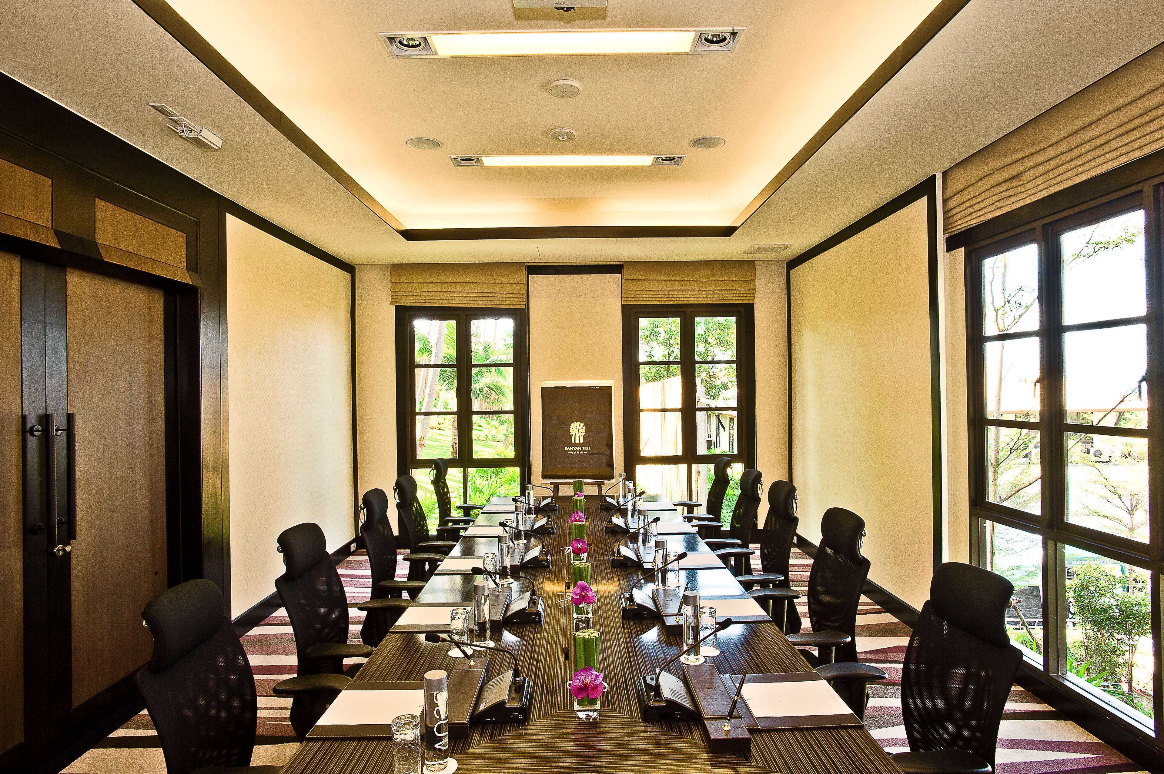 A conference room with a long table, chairs, and a projector screen.