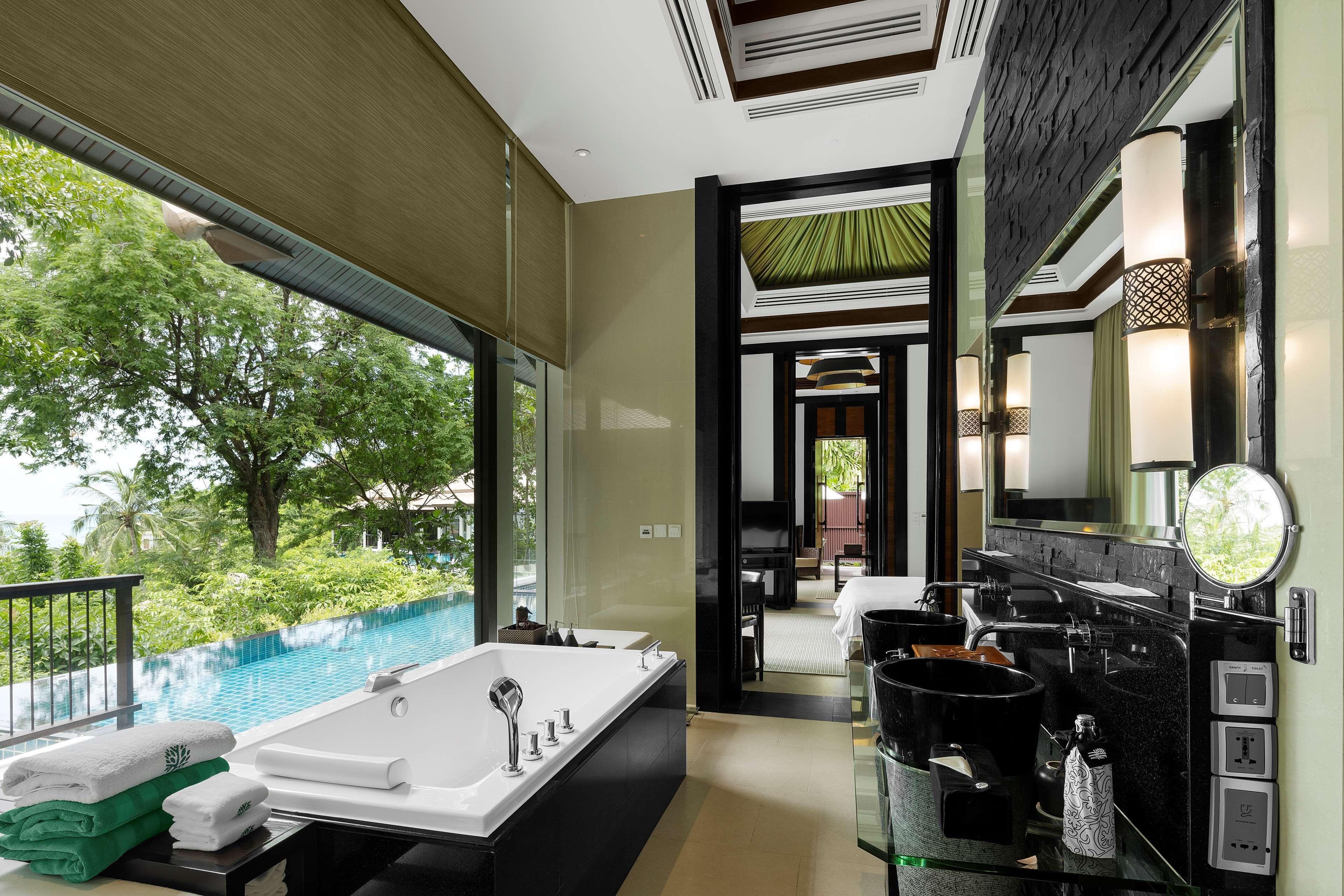 A modern bathroom with a large bathtub, a vanity with a mirror, and a view of a swimming pool.