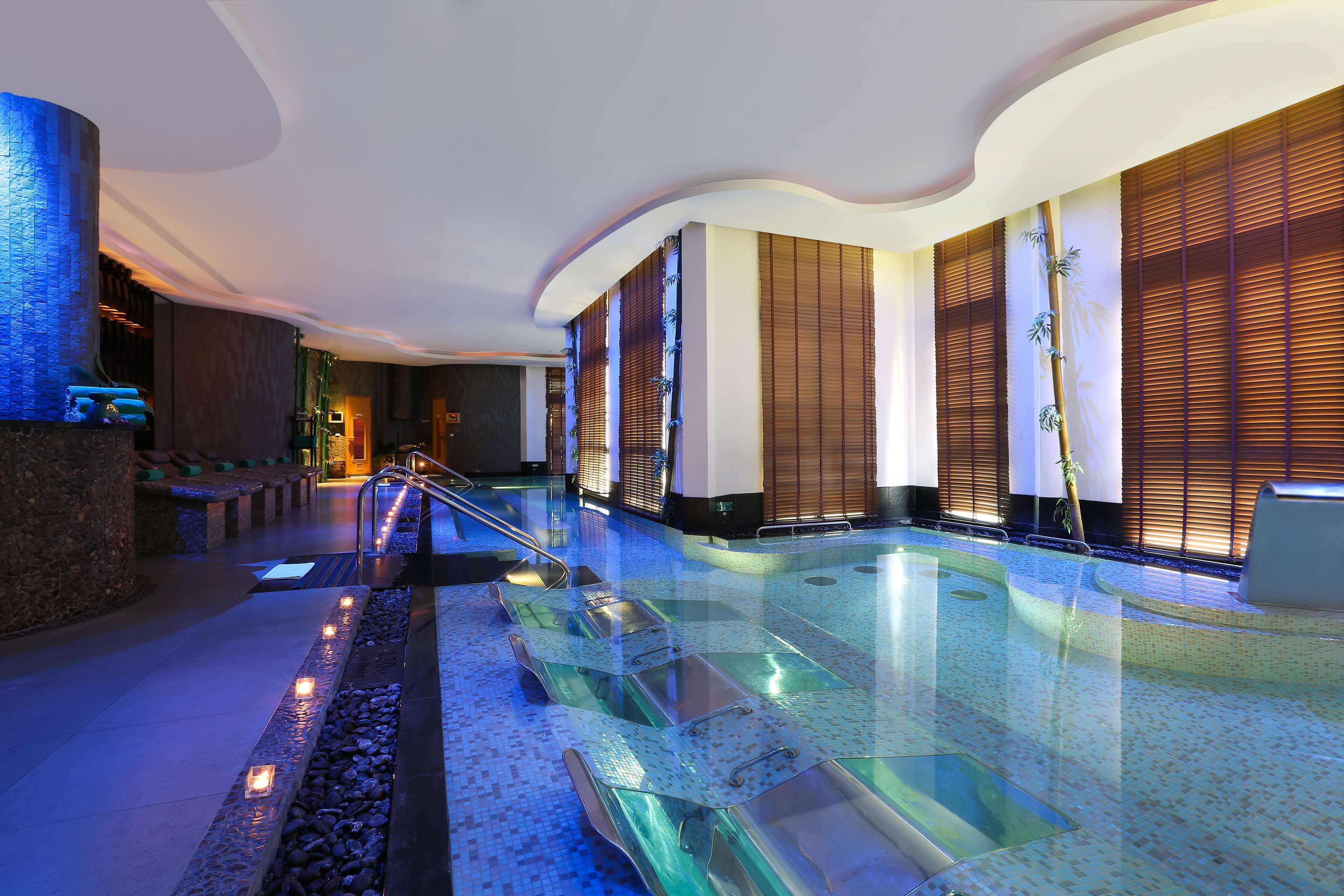 A modern indoor pool area with glass railings, a pebble-lined walkway, and ambient lighting.