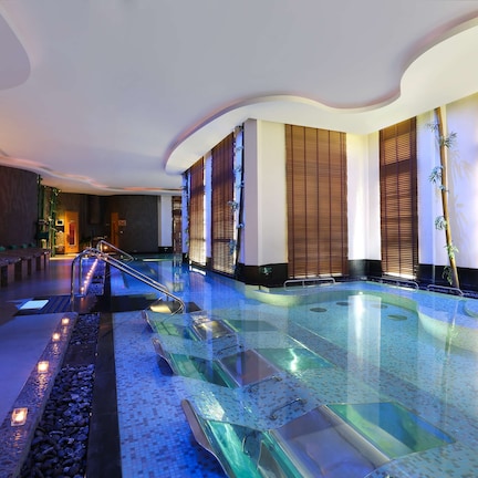 A modern indoor pool area with glass railings, a pebble-lined walkway, and ambient lighting.
