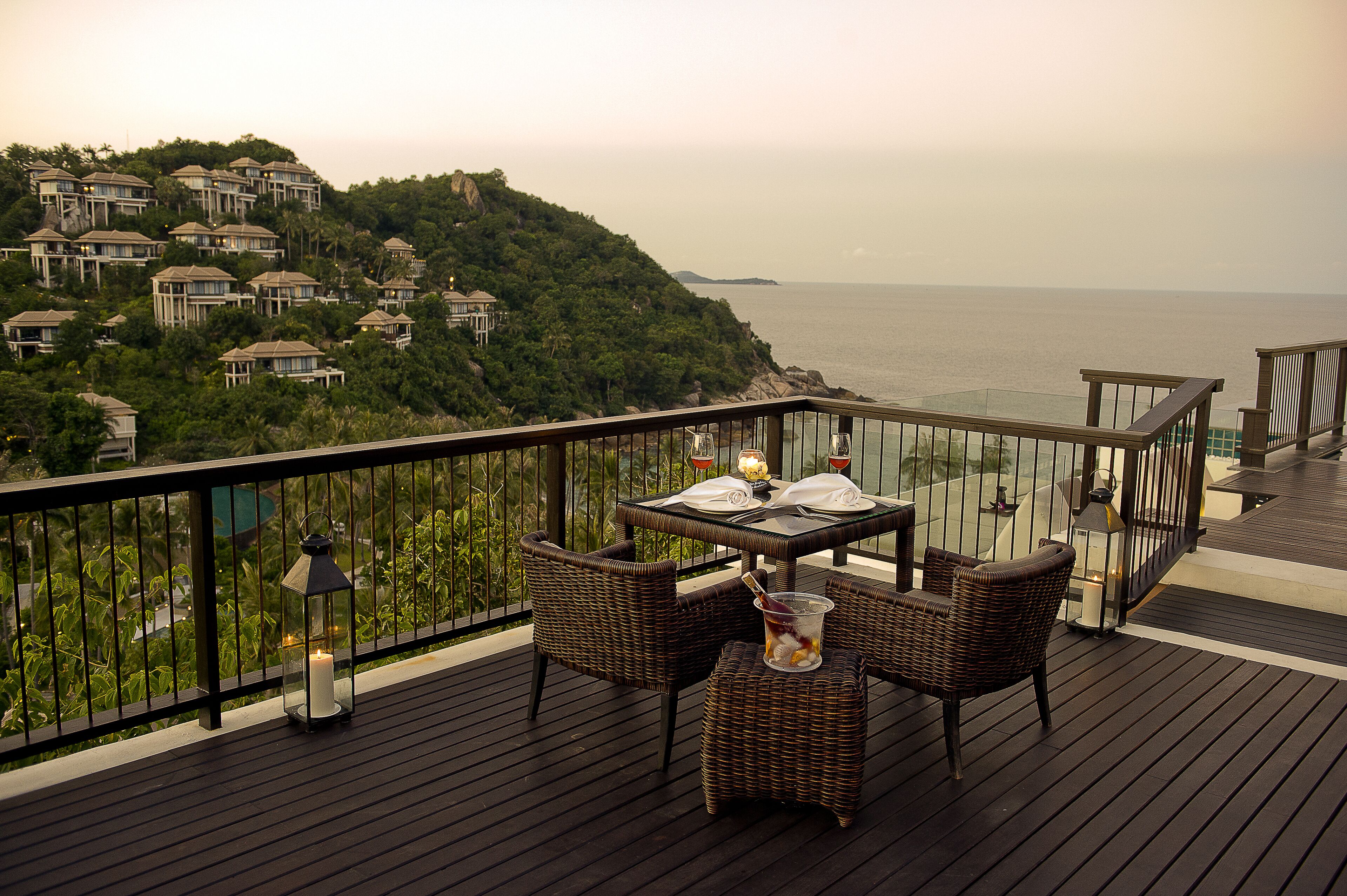 A deck with a table set for two, wicker chairs, and a candle.