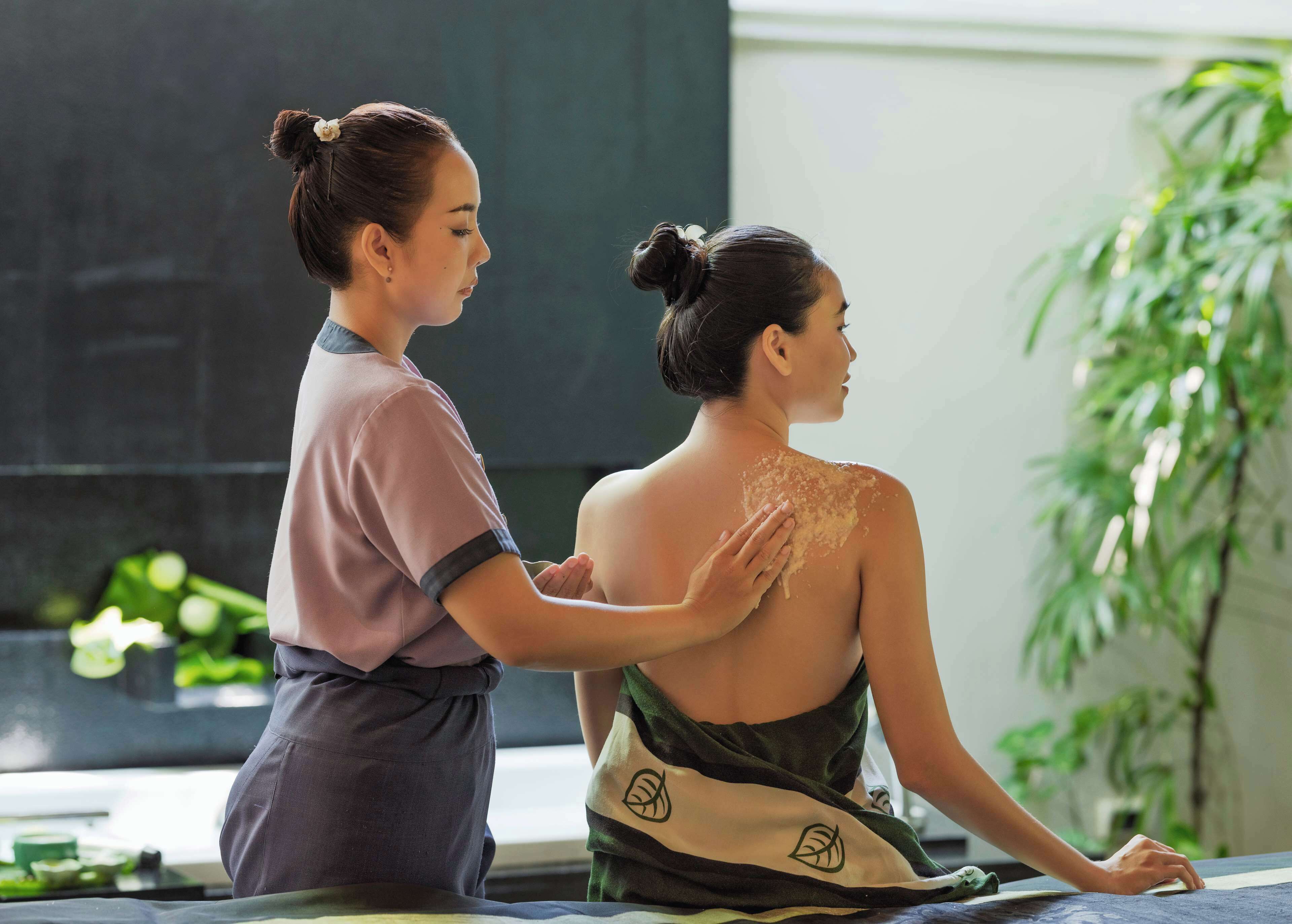 A person receiving a massage in a room with a large window and a plant.