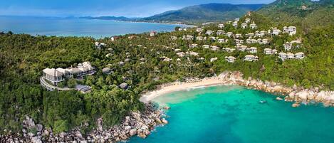An aerial view of a coastal resort with multiple villas, a beach, and a rocky shoreline.