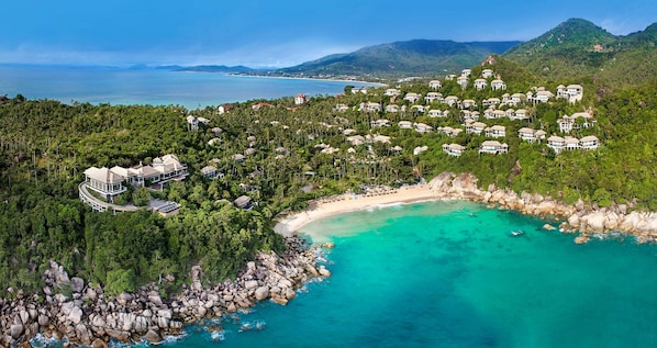 A coastal resort with beachfront villas, a sandy beach, and a rocky shoreline.