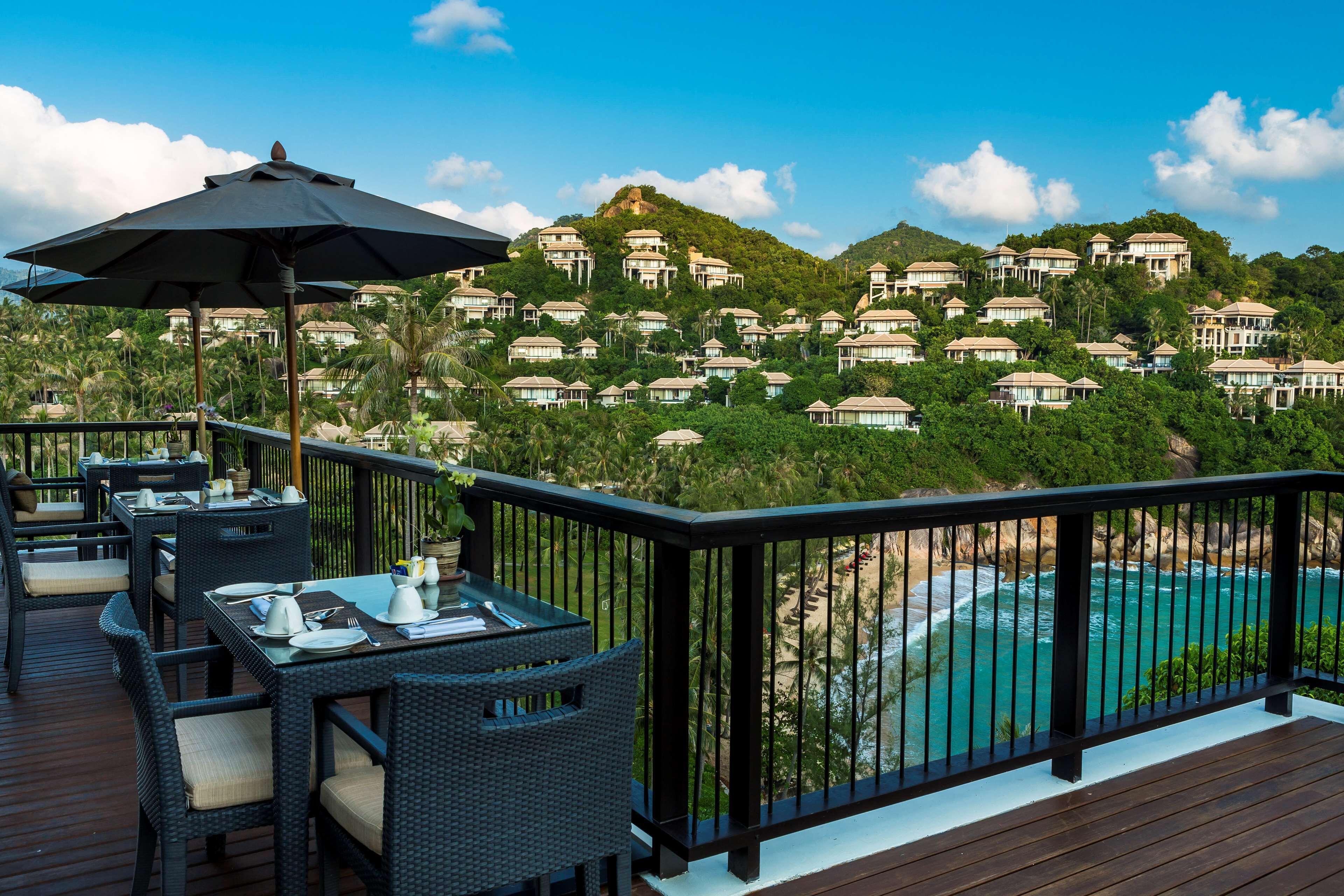 A deck with outdoor seating, overlooking a beach and a resort with multiple buildings.