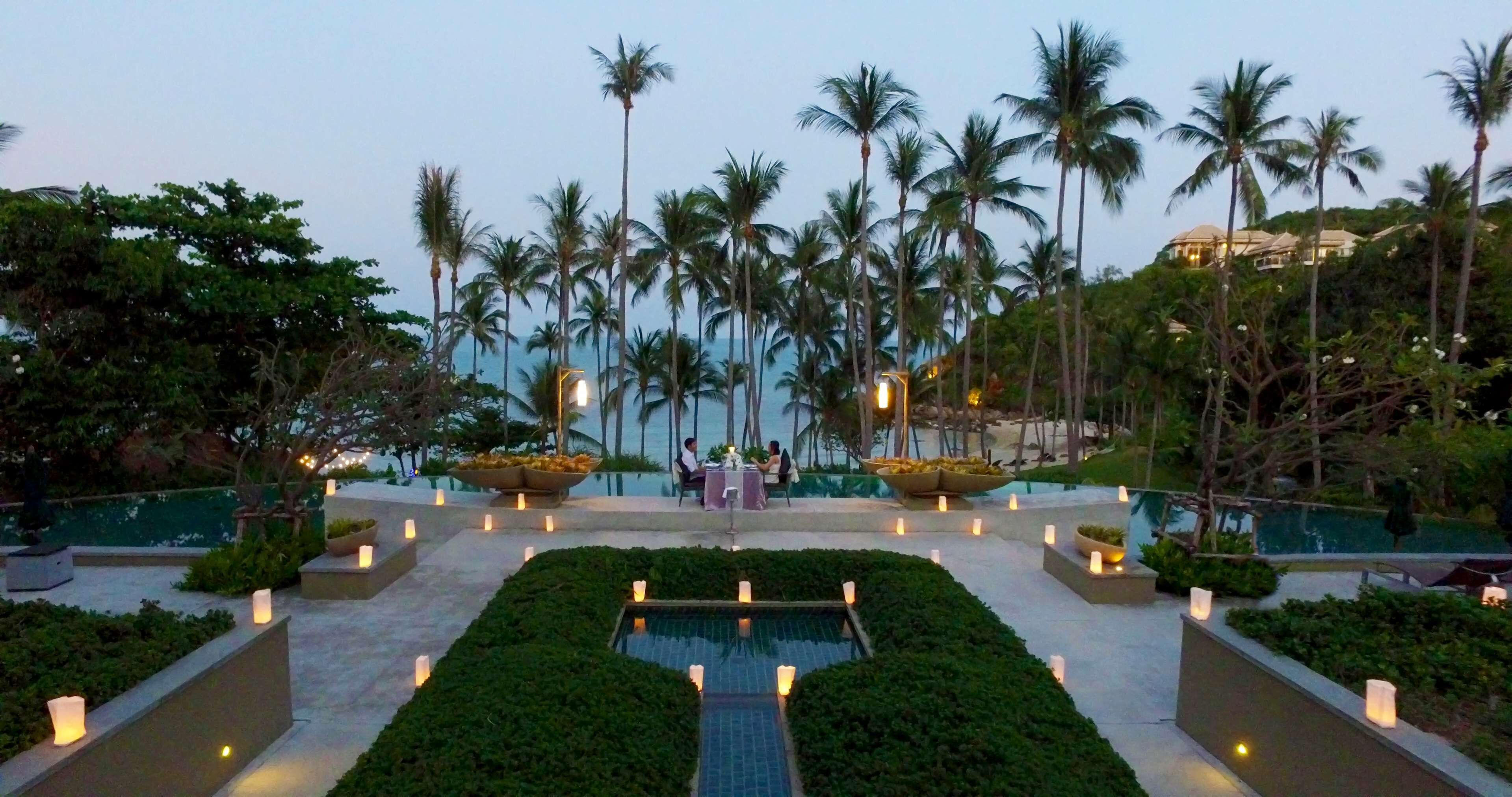 Un área de piscina con un conjunto de asientos y velas, rodeada de palmeras.