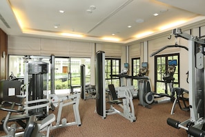 A well-lit gym with various exercise machines, large windows, and a view of greenery outside. - Banyan Tree Samui (Koh Samui)