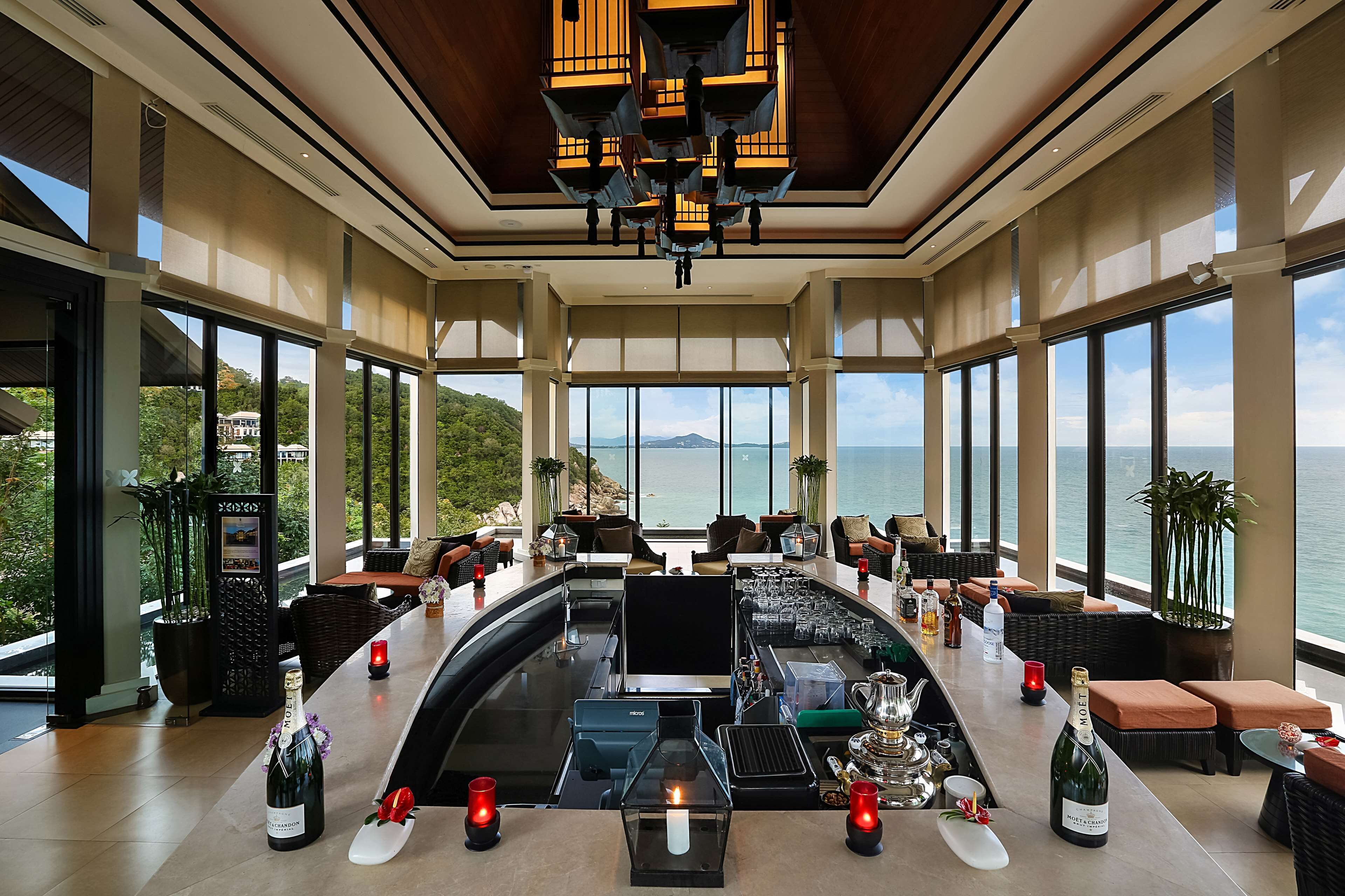 A spacious bar area with a view of the sea, furnished with sofas and a high ceiling with modern lighting.