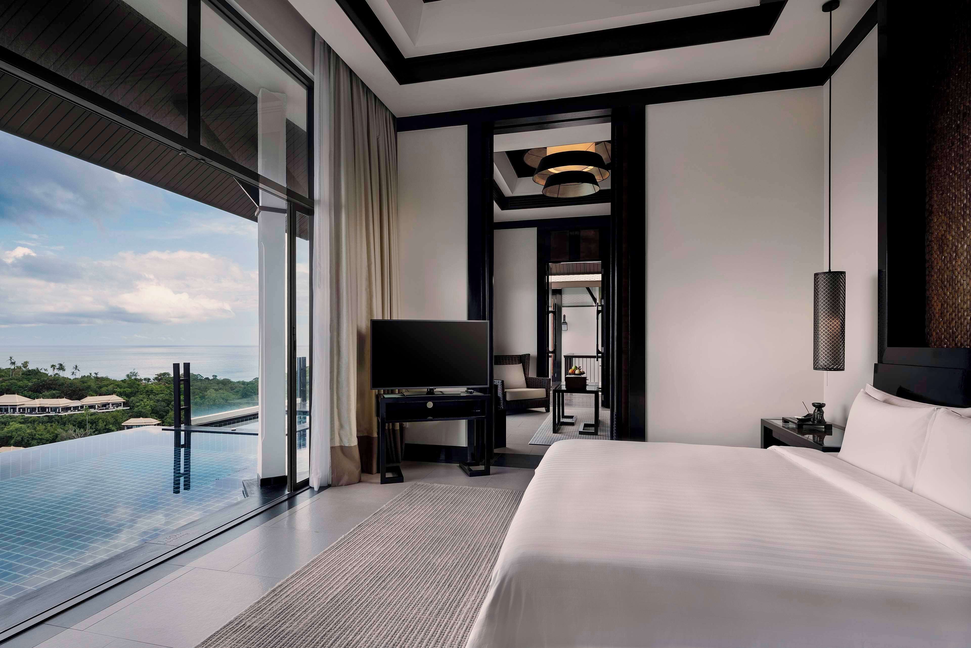 Habitación de hotel moderna con una cama grande, televisión y vistas a una piscina y zonas verdes.