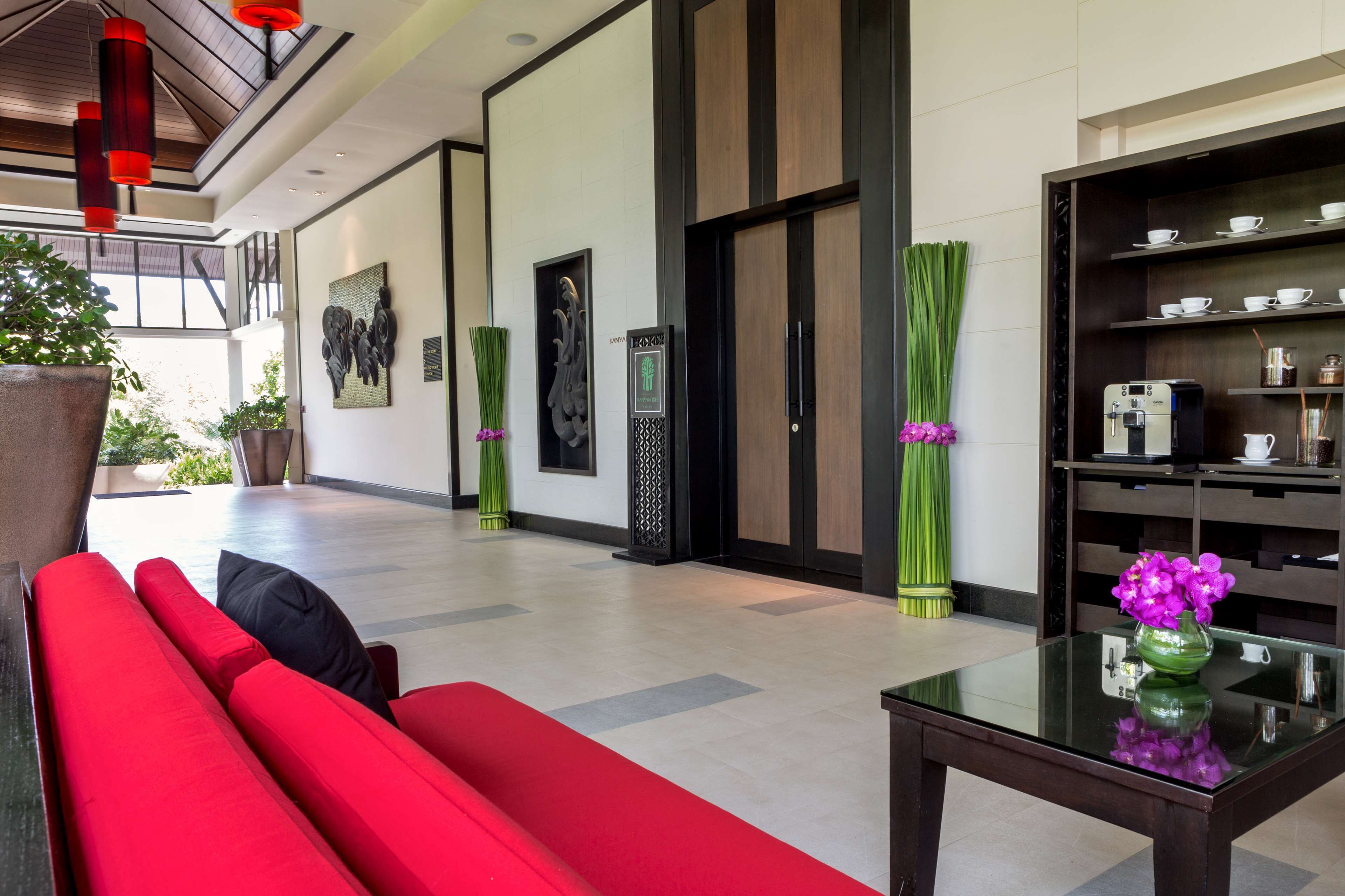 A hotel lobby with a red sofa, a coffee machine, and a vase with purple flowers.