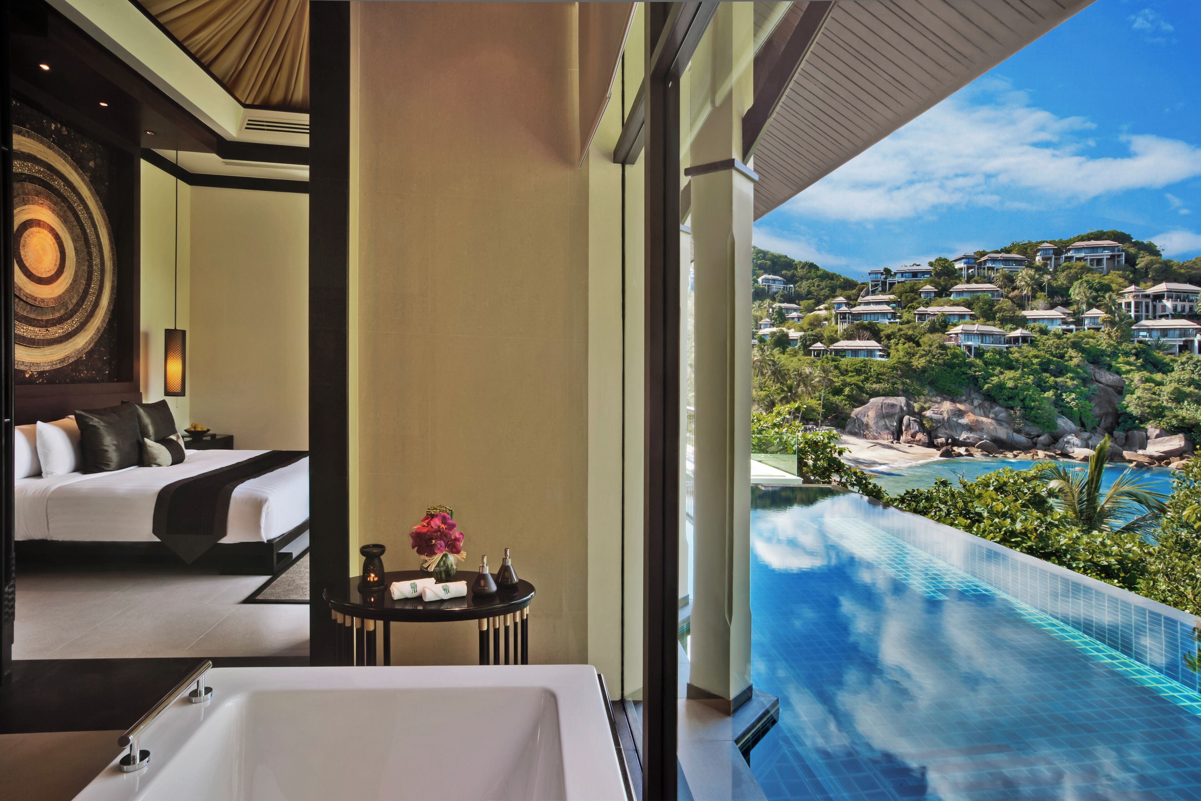 Habitación de hotel con una cama grande, baño con bañera y vista a una piscina y residencias en la colina.