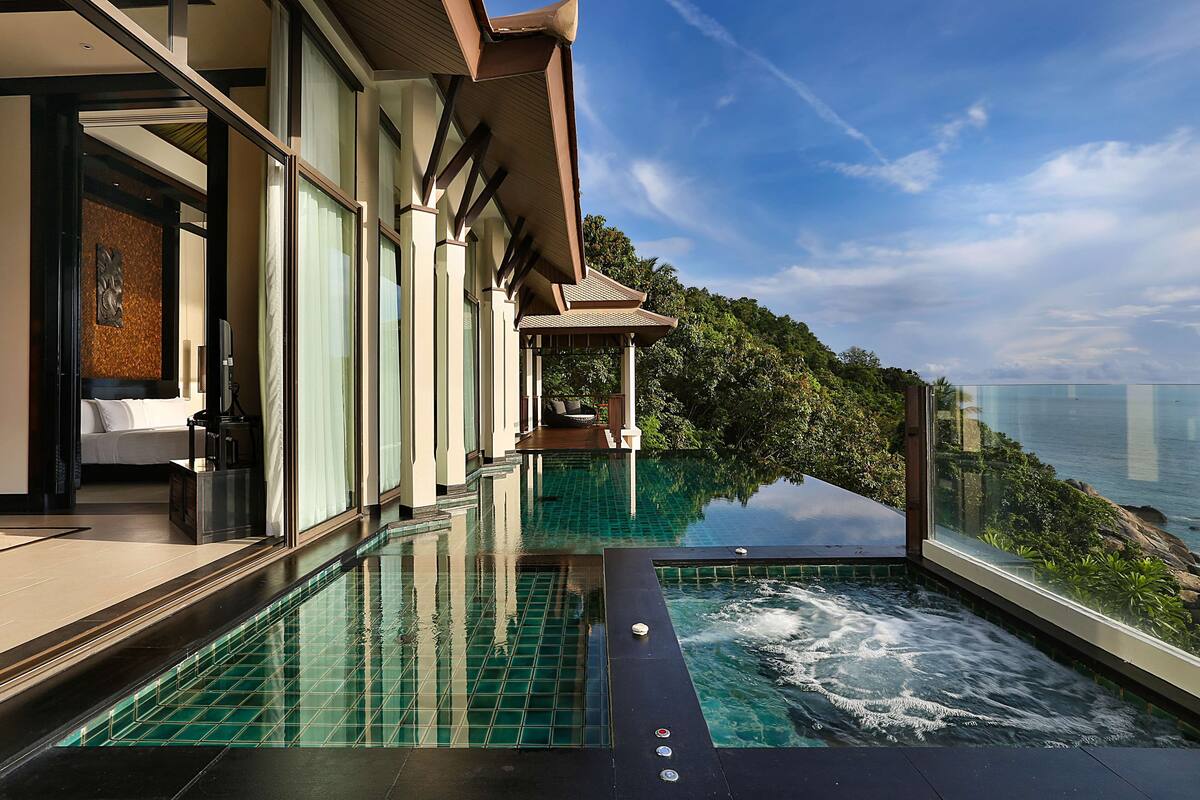 A modern infinity pool with a glass edge, a private outdoor seating area, and a view of the ocean.