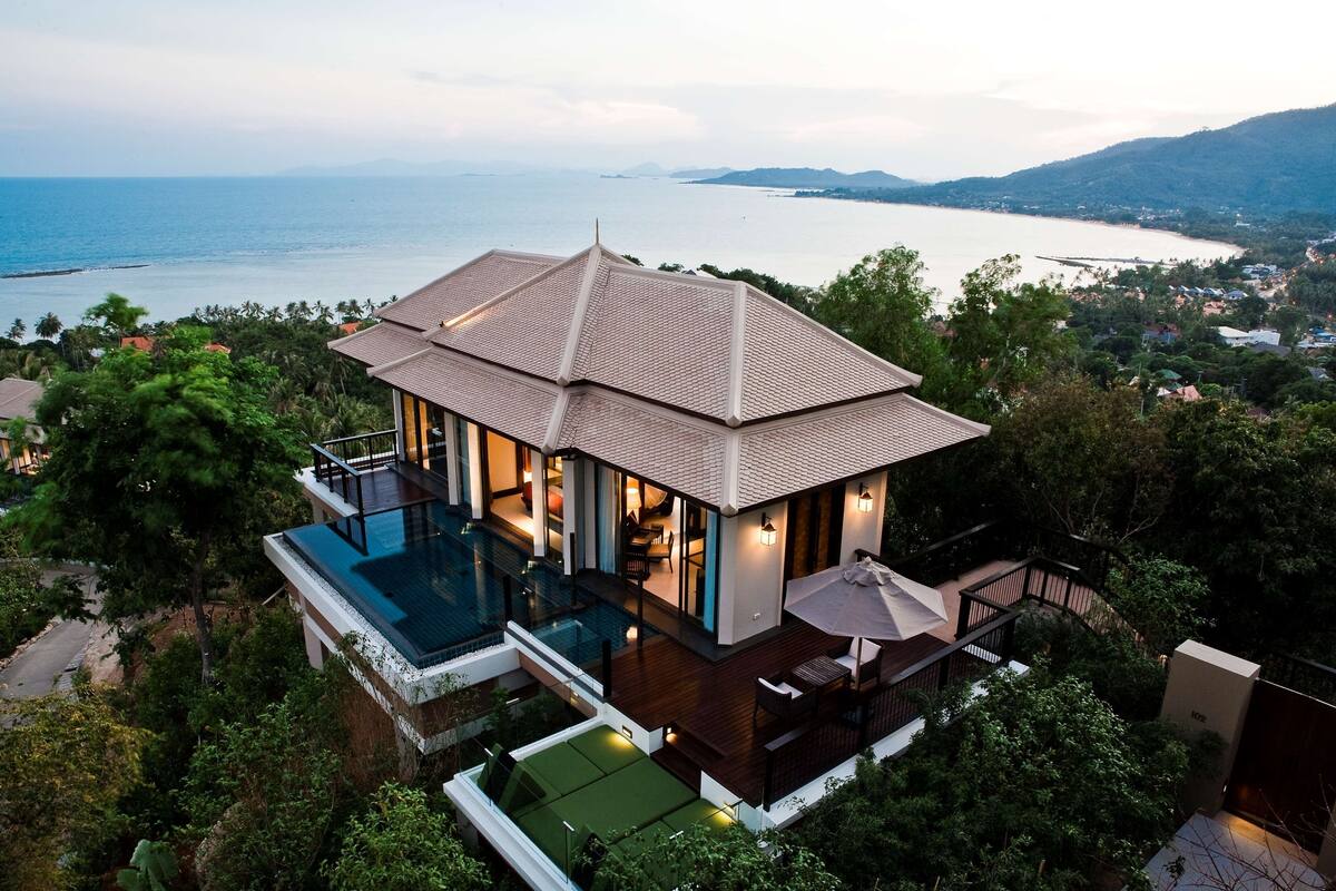 A modern house with a swimming pool, a deck, and a view of the sea.