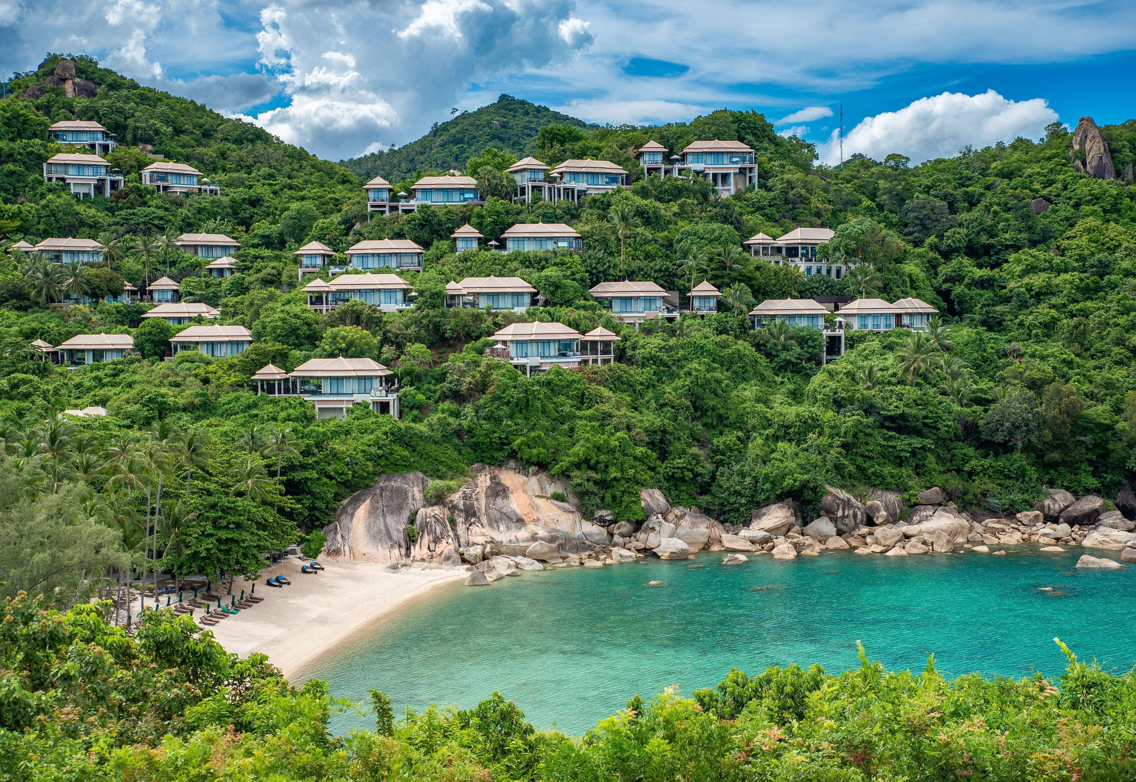Un complejo turístico en una ladera con varias edificaciones tipo bungalow, una playa y un litoral rocoso.