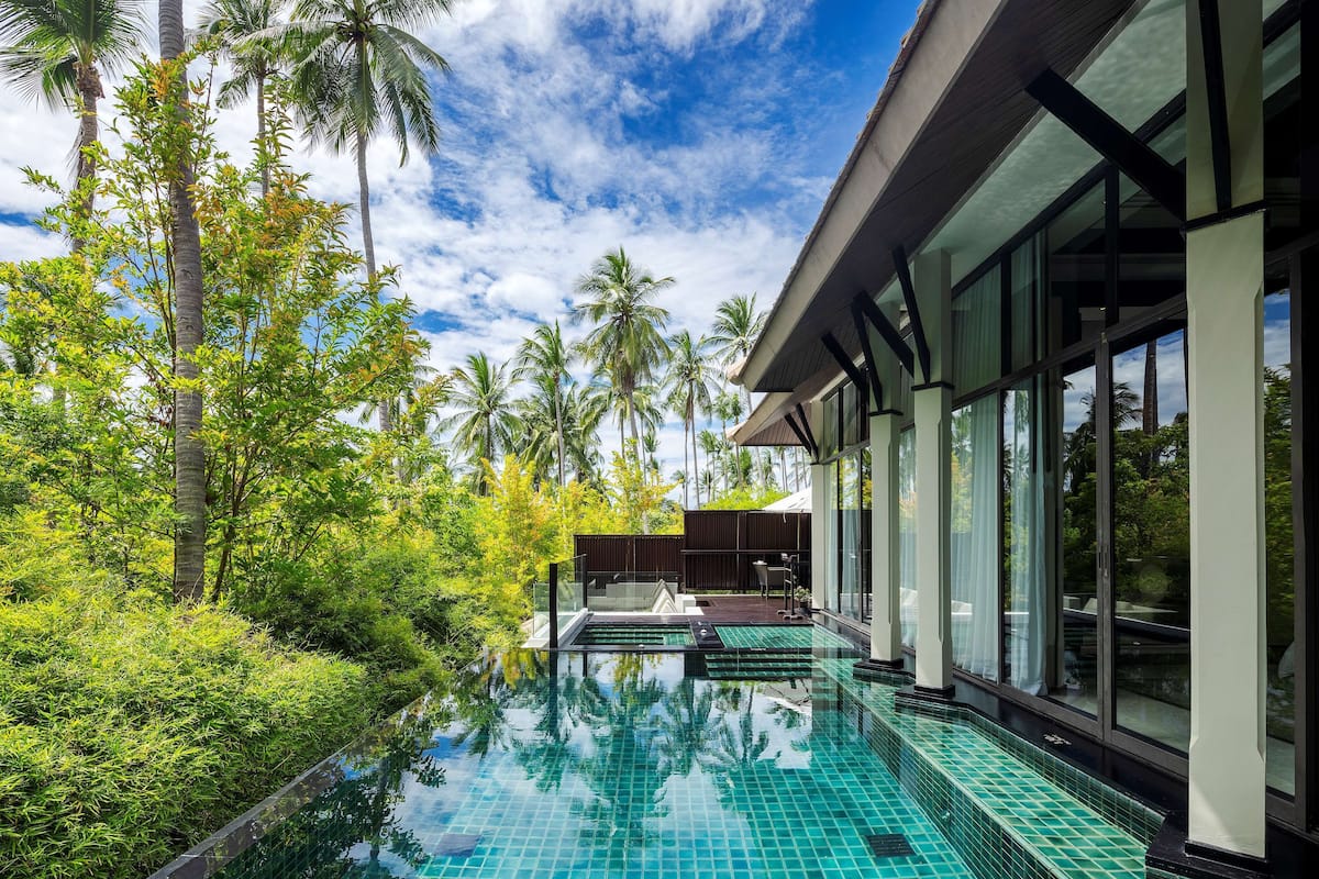 A modern pool area with clear blue tiles, surrounded by lush greenery and tall palm trees.