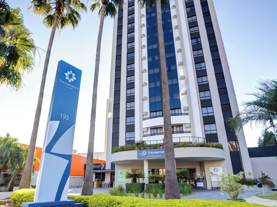 A modern building with a prominent blue sign, palm trees, and a well-maintained garden.