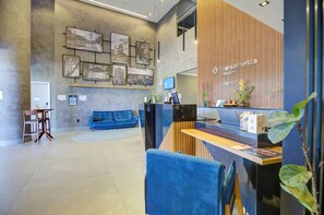 A modern reception area with a blue sofa, a reception desk, and a wall with framed pictures. - Transamerica Executive Sorocaba (Sorocaba)